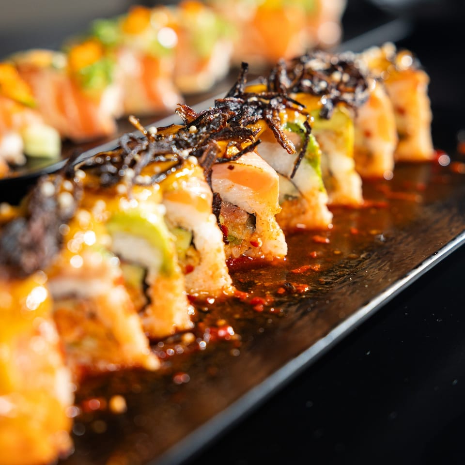 Close-up of Shogun Sushi's spicy sushi rolls with dark seaweed and sauce on a black plate.