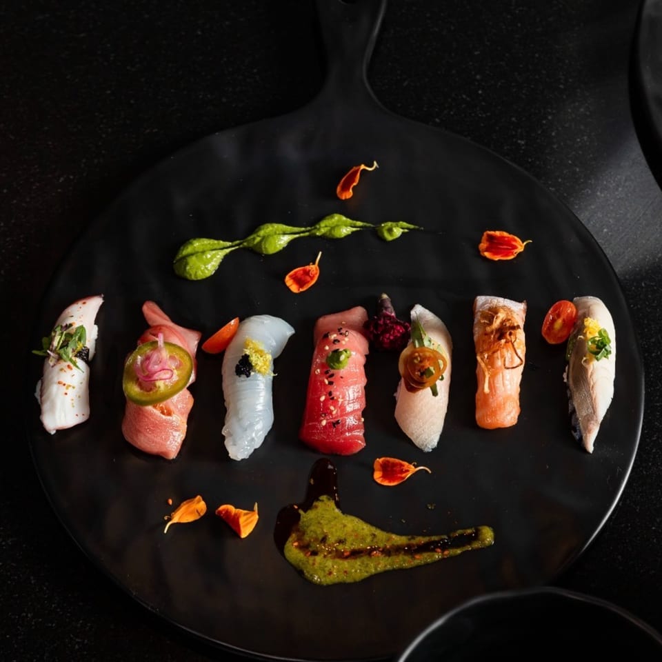 Assortment of Shogun Sushi nigiri with various toppings and green sauce on a black plate.