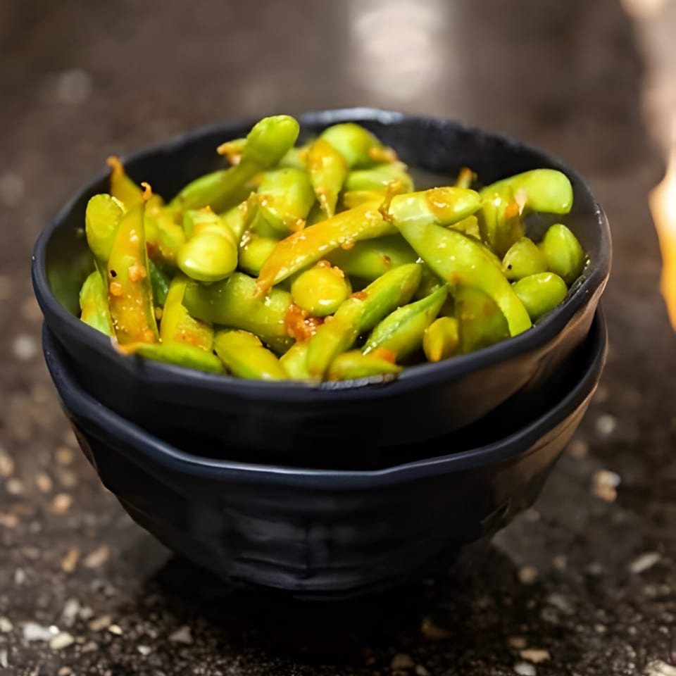 Two black bowls filled with vibrant green edamame, lightly seasoned, on a dark textured surface.